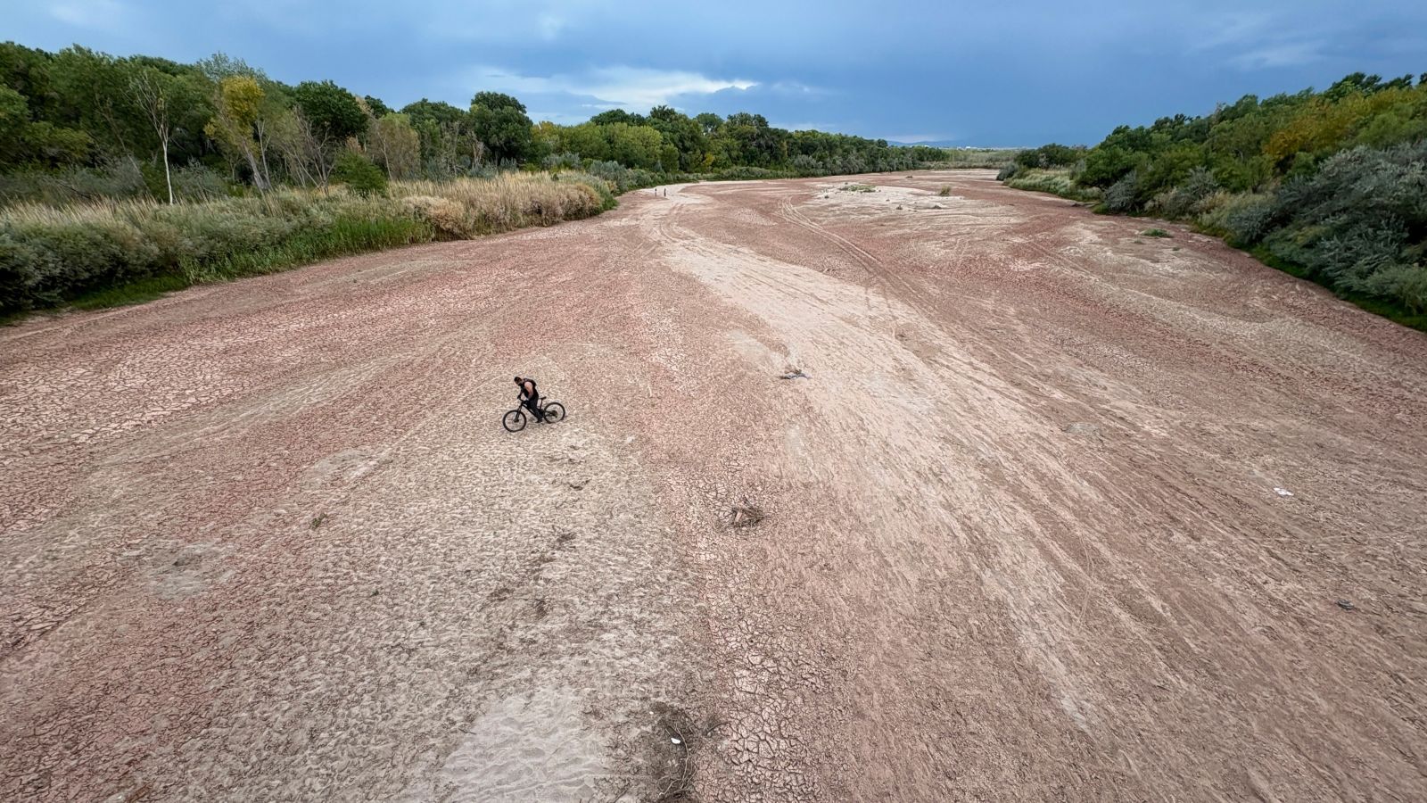A cyclist rides across a dry riverbed