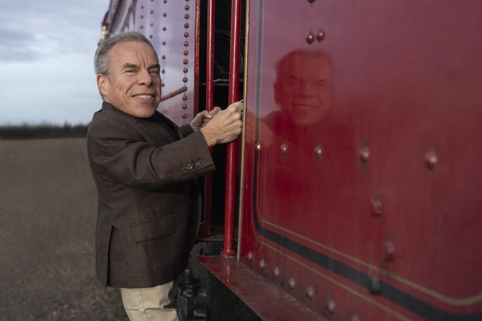 Warwick Davies standing on the side of a red train Warwick Davies standing on the side of a red train