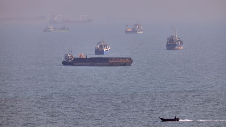 A small boat sails past cargo ships and other commercial vessels anchored in the Strait of Hormuz off Bandar Abbas, Iran, Wednesday, Aug. 5, 2026.