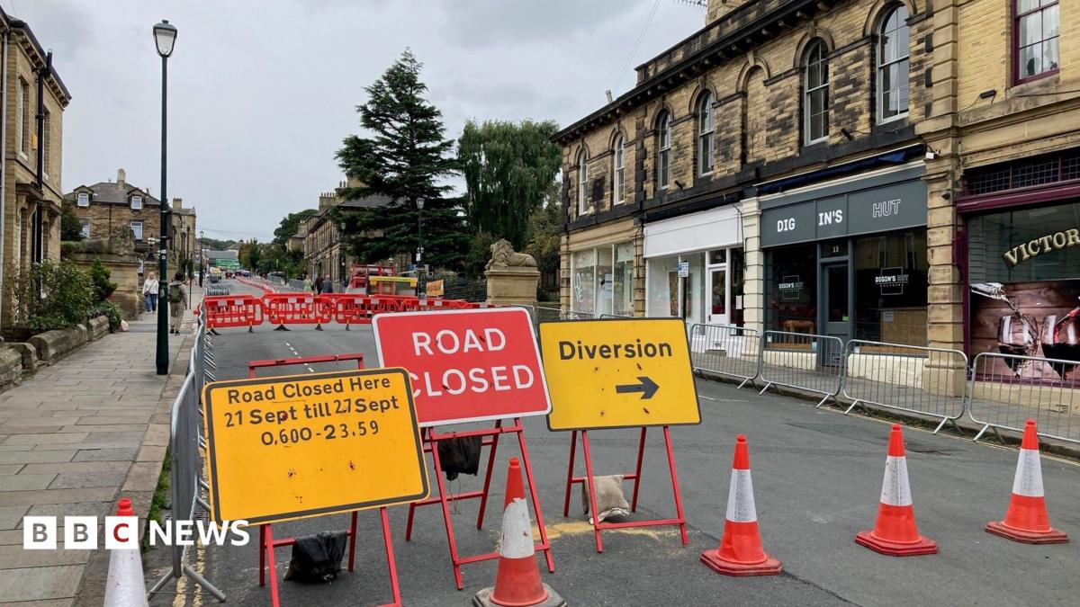 Yellow and red road signs showing road closure times and pointing to a diversion. There are red and whites barriers and traffic cones closing off the road.