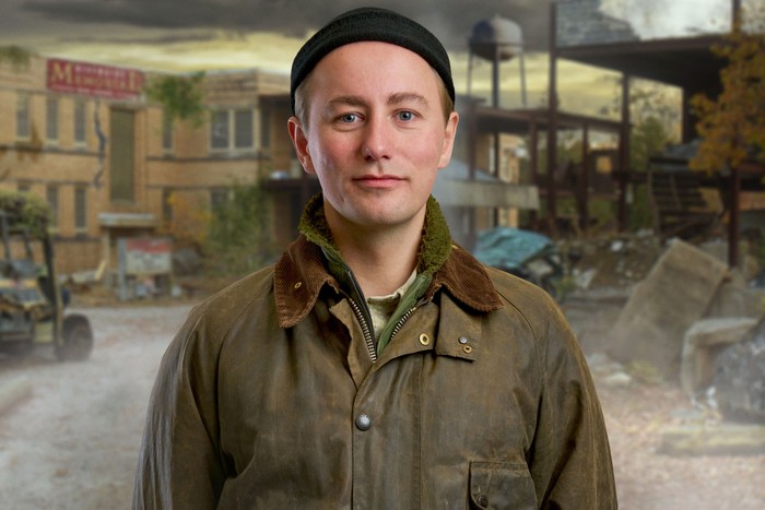A man wearing a green jacket and black hat, smiling.