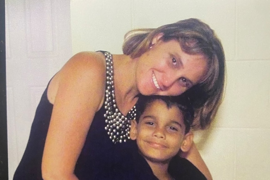 A woman leans over a young boy, both smiling at the camera.