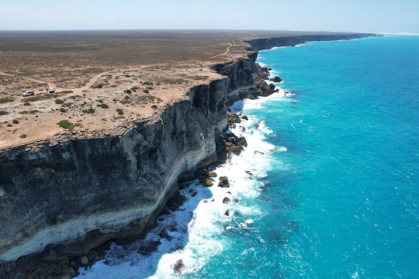 A cliff face with a bright blue sea crashing against it