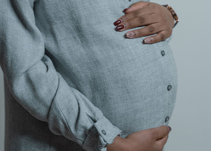 Close-up of a pregnant woman holding her belly, discussing symptoms with doctors who stop and stare.