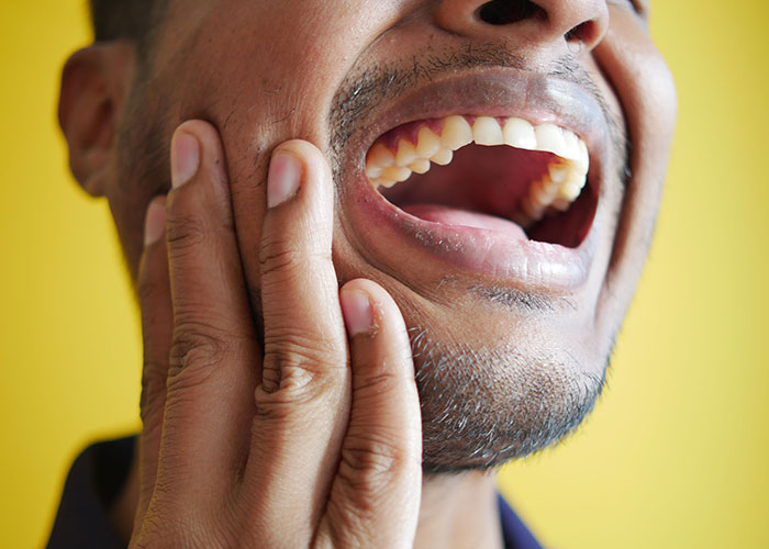 Man showing symptoms of tooth pain, holding his cheek as doctors stop and stare.