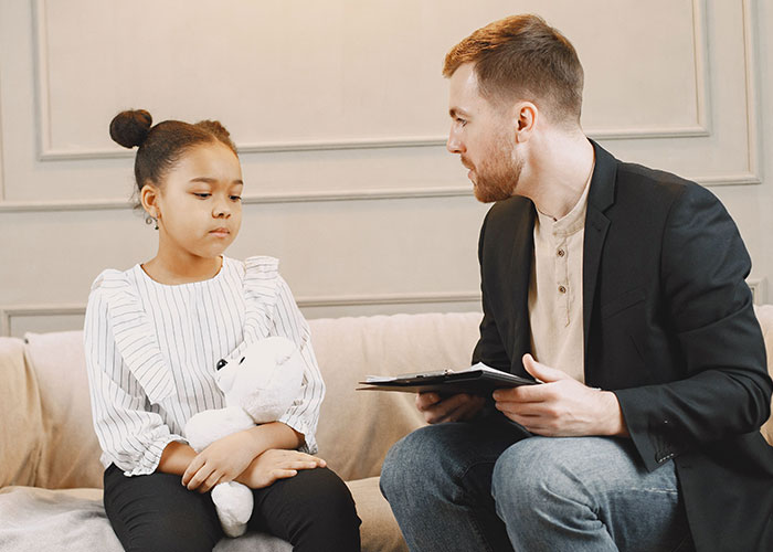 A young girl with a teddy bear talking to a doctor, sharing her symptoms. Doctors often stop and stare at unusual symptoms.