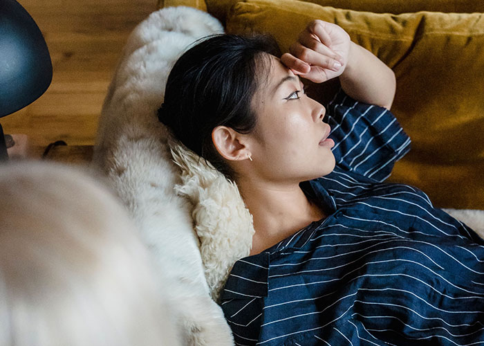 Woman lying down, experiencing symptoms of a headache, as doctors stop and stare.