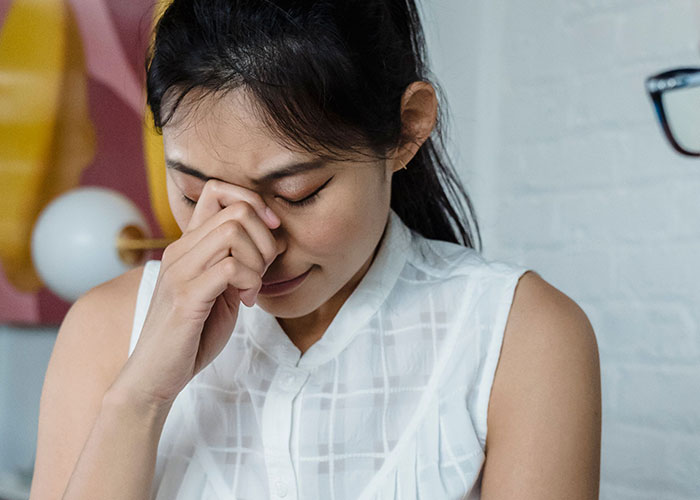 A woman experiencing symptoms of discomfort, rubbing her eyes with a pained expression. Doctors may stare at these symptoms.