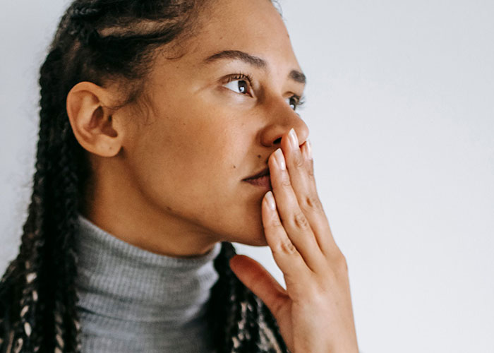 A woman with braided hair and a gray turtleneck covers her mouth, contemplating normal symptoms that puzzle doctors.