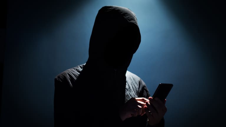A hooded man holding a phone. 