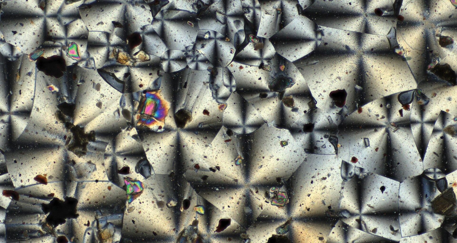 A microscopic view of the kaleidoscope-like crystal structures of two NASA-made material samples, a gray sample on the left and a reddish sample on the right.