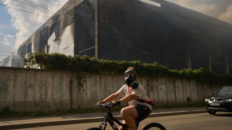 A Kyiv resident wears a gas mask as he cycles past a drone-attacked warehouse.