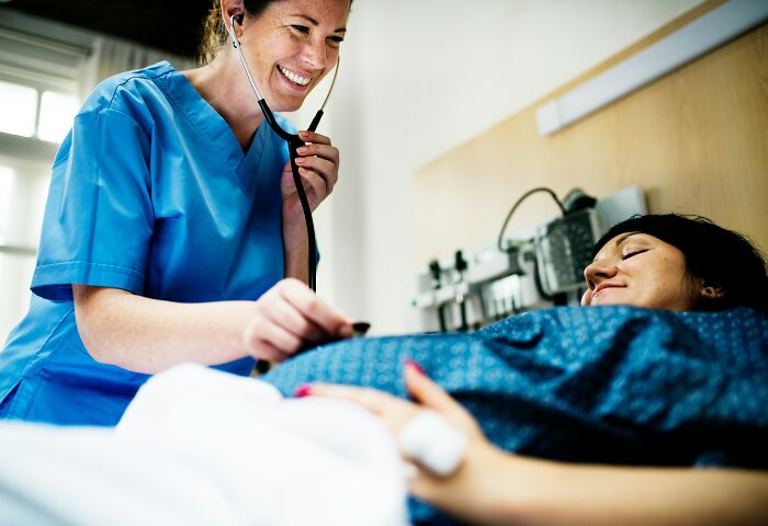 A smiling medical worker using a stethoscope to check a happy pregnant patient in a hospital