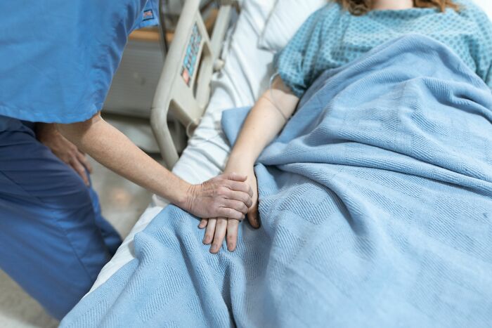 A compassionate medical worker holding the hand of a patient lying in a hospital bed