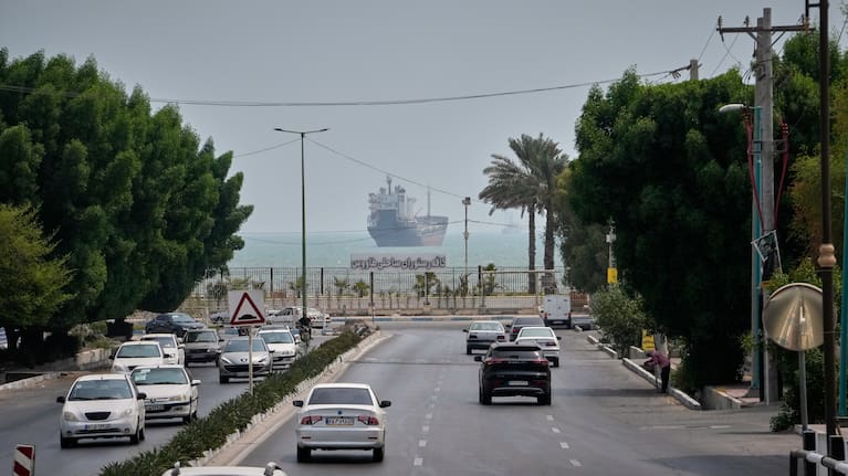 Traffic moves along an avenue as a commercial vessel lies anchored in the Strait of Hormuz off Bandar Abbas, Iran