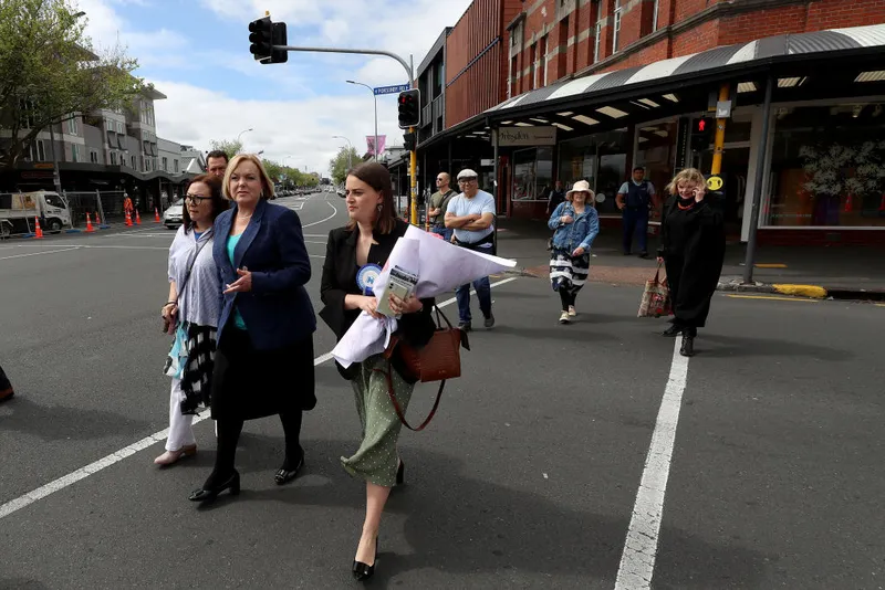 Women cross a street, one holds a bouquet of flowers