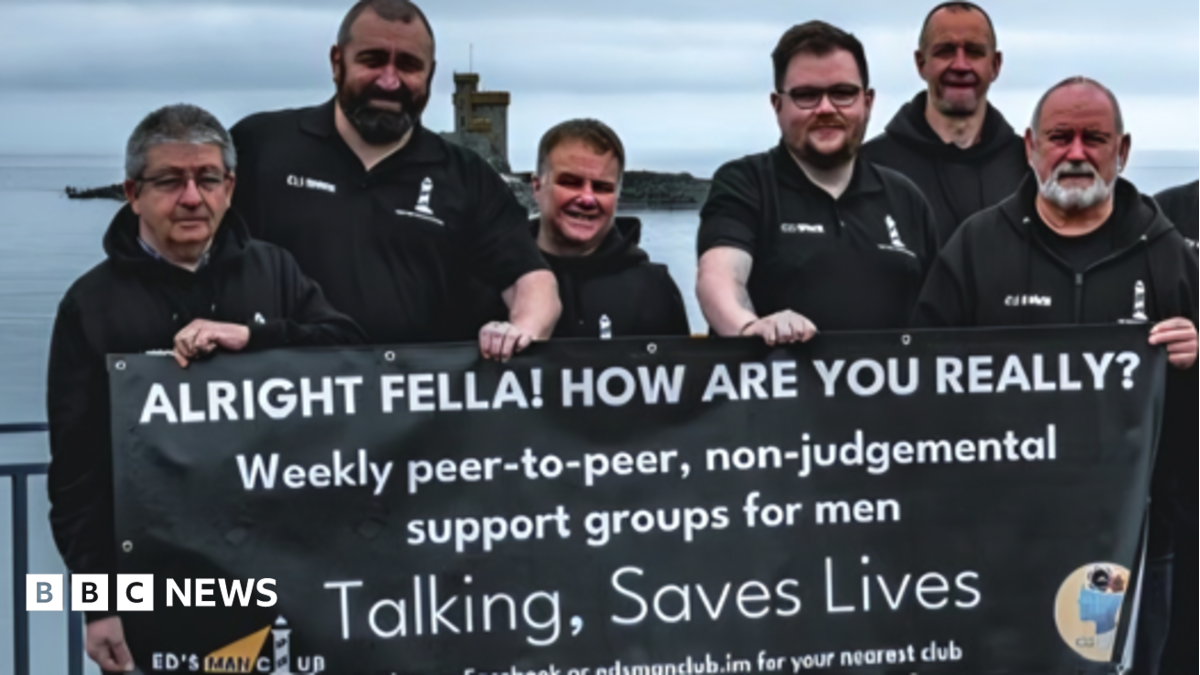 A group of men in black tops standing on Douglas Promenade holding a banner about the support services that says talking saves lives.