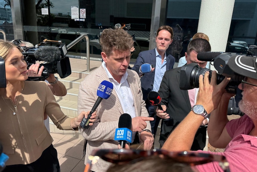 Reporters and camera operators point microphones and cameras at Mathew Cuskelly.