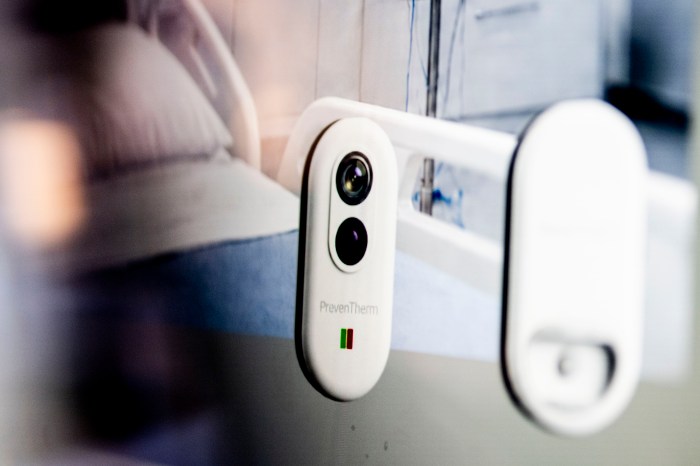 A white device with two camera lenses mounted on the rail of a hospital bed.