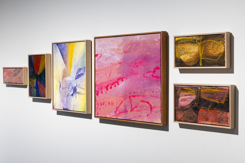 Six framed abstract images in browns and pinks and blues hang on a white wall.