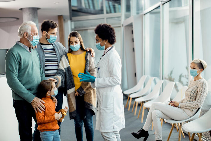 Female doctor in a face mask speaking with a family of patients in a hospital waiting room.