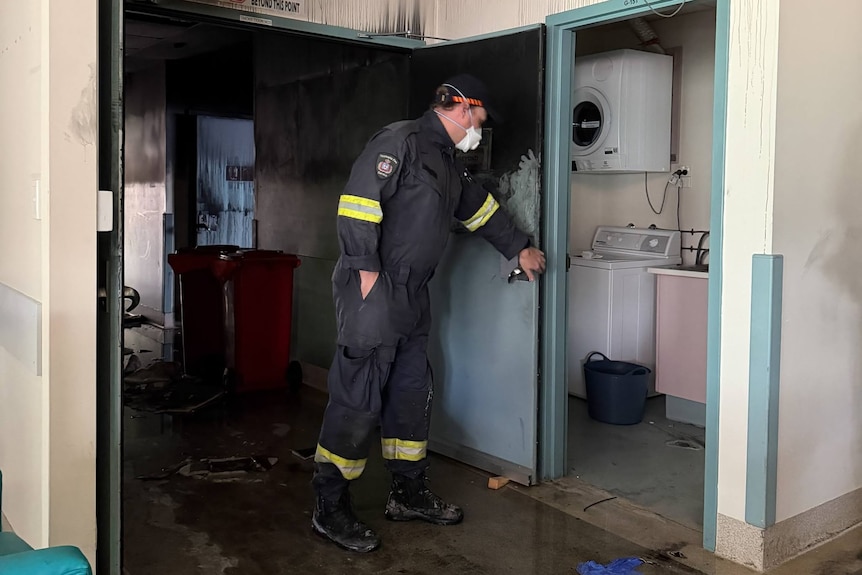 Man in uniform inspects fire and smoke damage to a building.