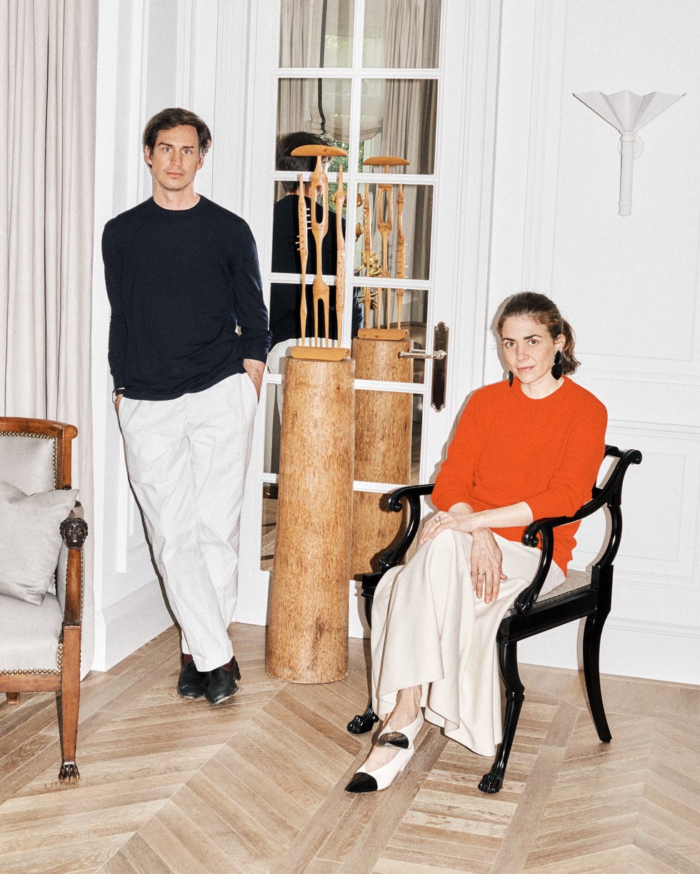 A man in a navy sweater and a woman in an orange top pose in a stylish interior with wooden accents and elegant decor.