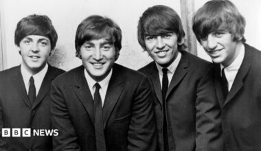 Black and white photograph of the Beatles who are wearing dark suits and ties with Ringo Starr on the far right of the picture