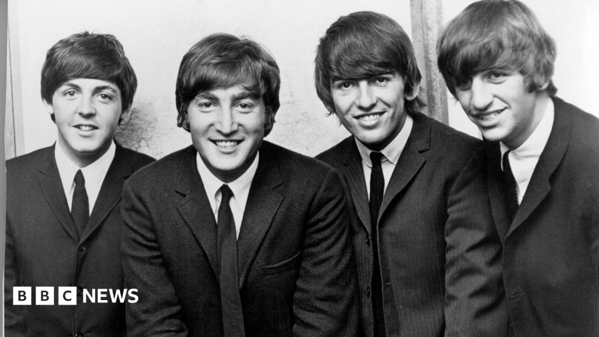 Black and white photograph of the Beatles who are wearing dark suits and ties with Ringo Starr on the far right of the picture