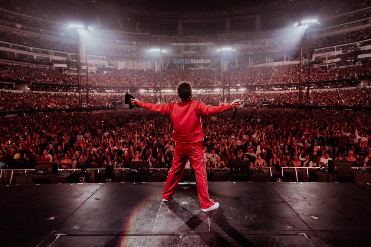 Bruno Mars onstage at SoFi Stadium in a red suit, arms flung out.