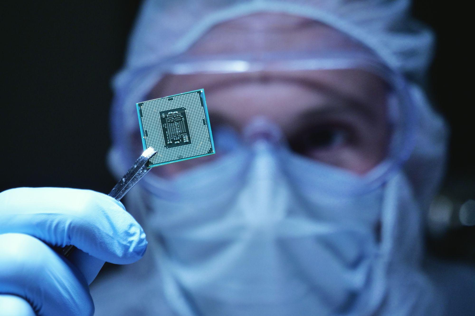 A technician in sterile protective gear is closely examining a microchip.