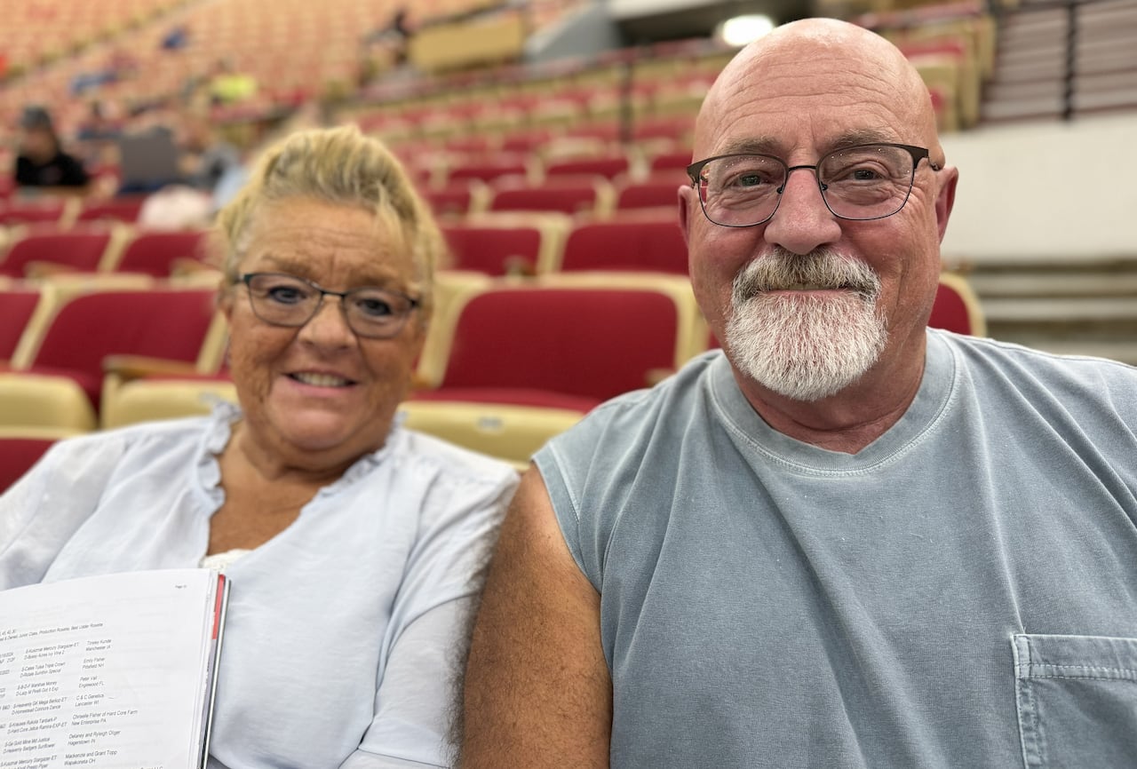 A middle-aged couple sit together in an arena, posing for a photo