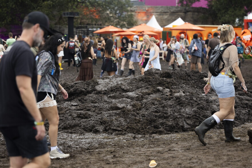 People walk by a large mud pile during a music festival.