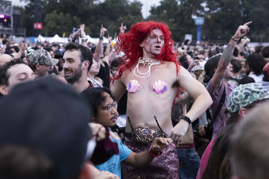 A man dressed as a mermaid jumps into the air in a crowd at a music festival.