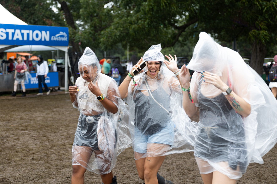 Three women wearing rain ponchos laugh as they walk on muddy ground.
