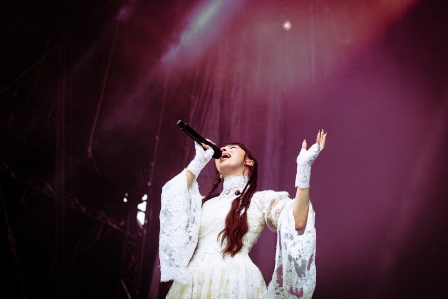 A woman looks up with one arm raised slightly while singing into a microphone on stage.