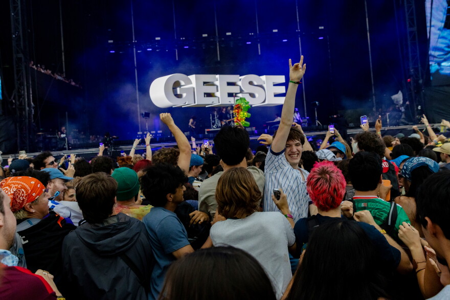 People mosh in front of a band. One man is turned toward the camera with his arm in the air as he smiles.