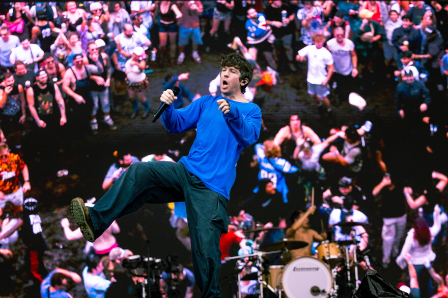 A man performs on a stage with a screen behind him showing an audience.