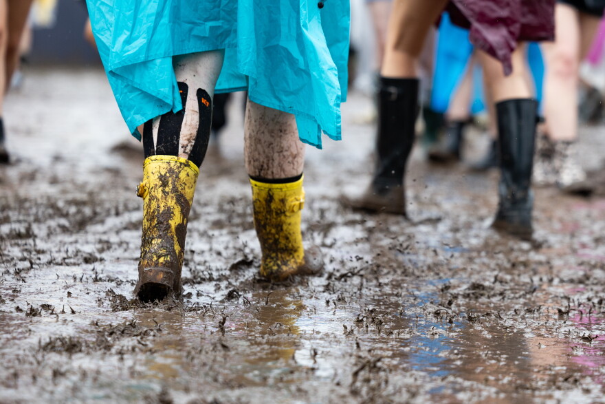 Two sets of boots, one yellow, are shown close up walking through wet mud.