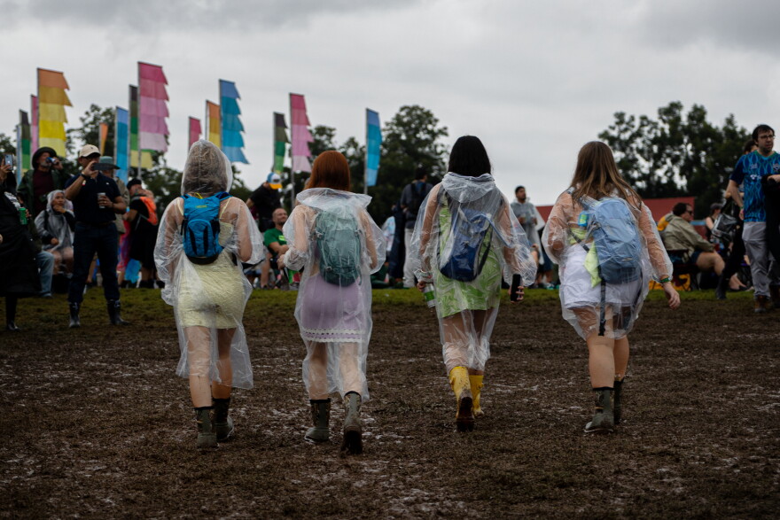 Four women are shown from behind with ponchos on walking across mud at a music festival.