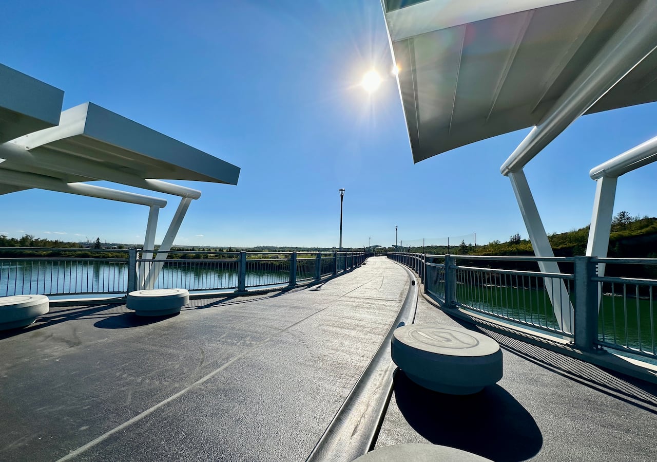 A smooth, new concrete path enters one end of a pedestrian bridge over water