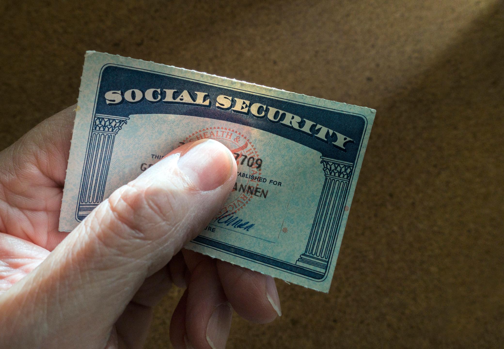 Hand holding a U.S. Social Security card against a plain brown background
