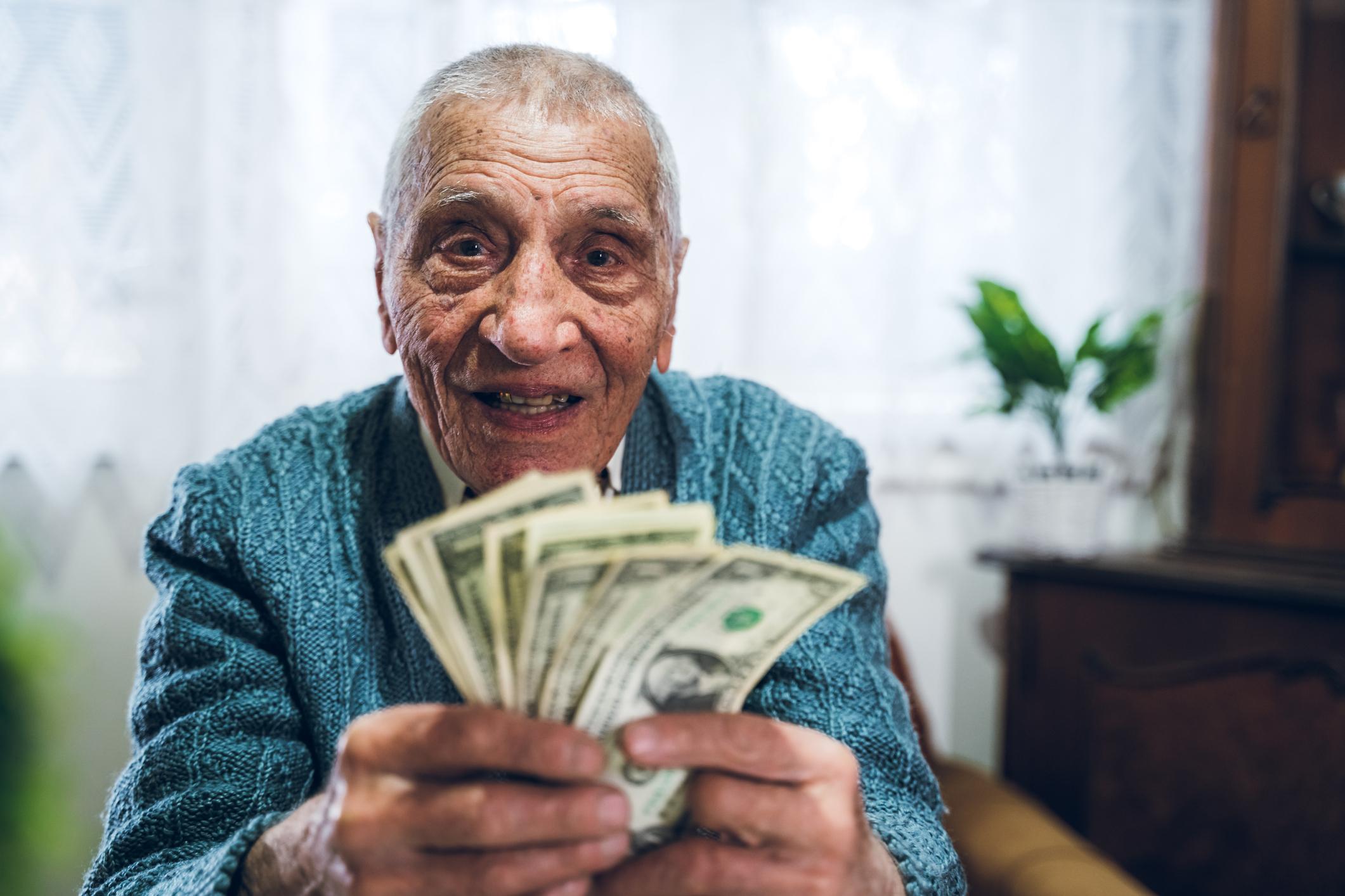 A smiling person is counting a fanned assortment of cash bills in their hands.