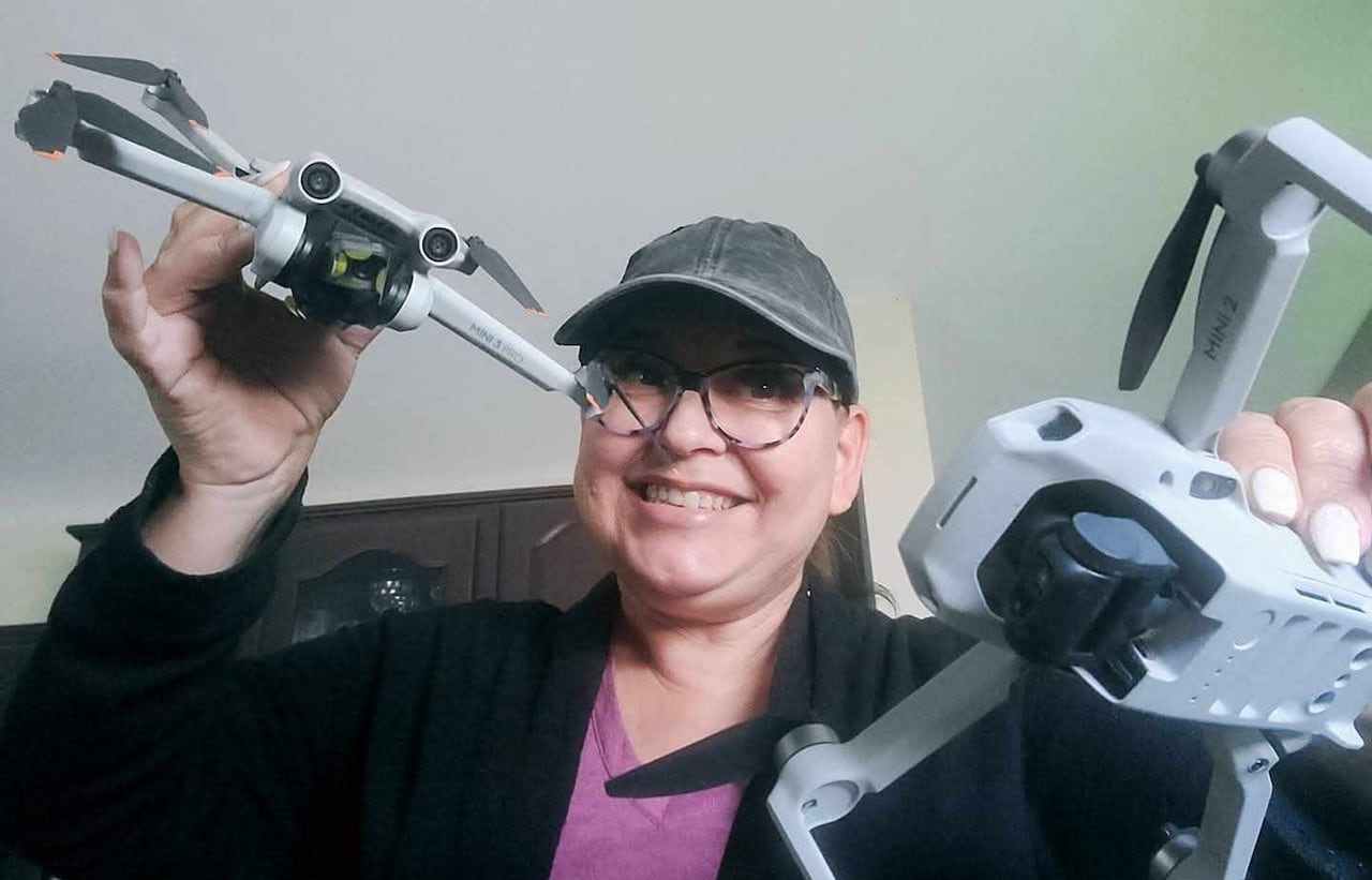 A smiling woman holds up two small drones.