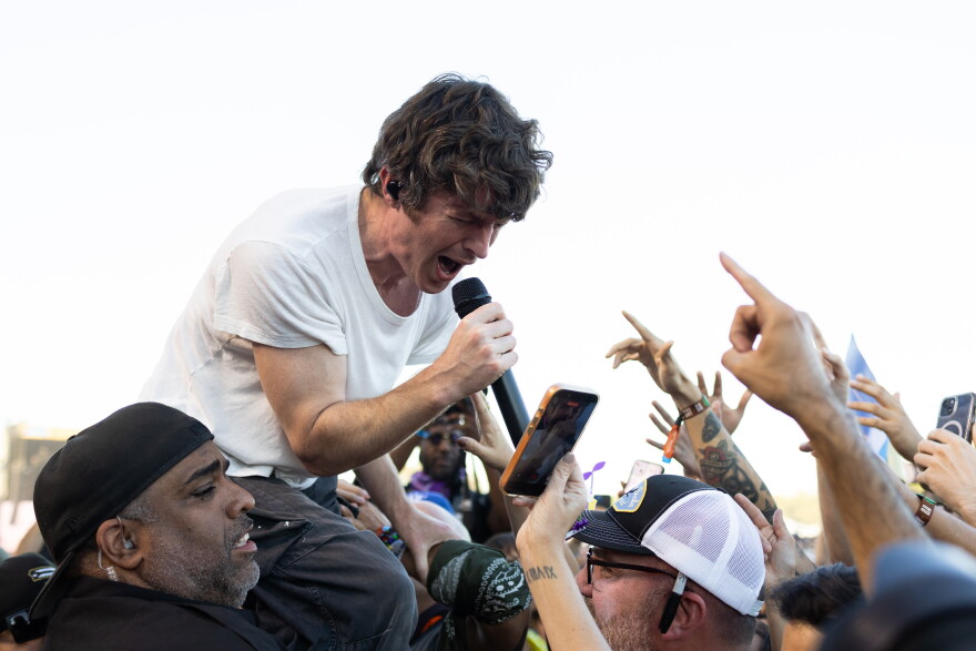 A man stands over a crowd with hands reaching toward him as he performs during a music set.