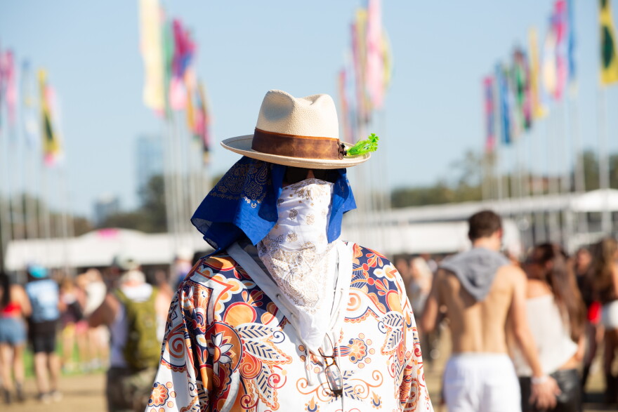 A woman wears a hat and a bandana covering her face at a music festival.