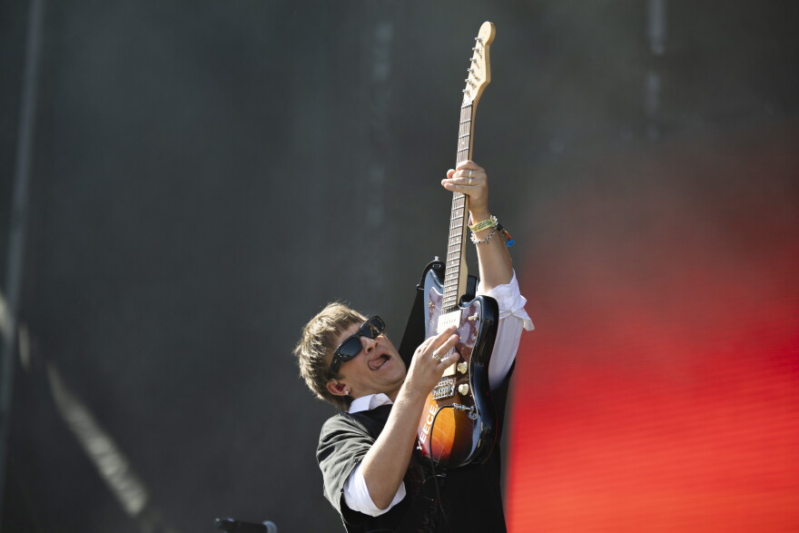 A man performing on a stage sticks out his tongue while holding his guitar in the air.