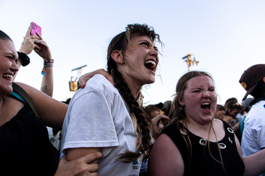 Two women sing along to a song while in a crowd at a musical performance.
