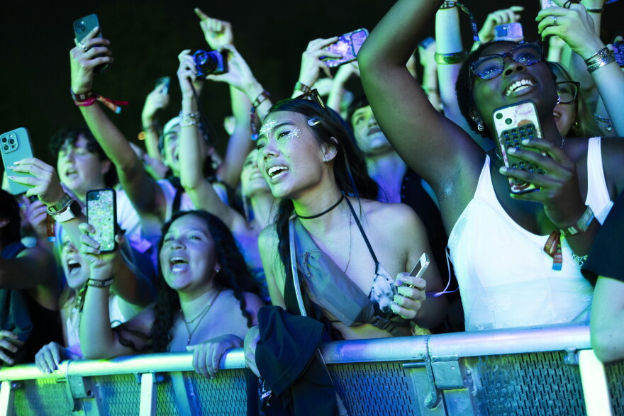 People stand at a barricade singing during a live music show.