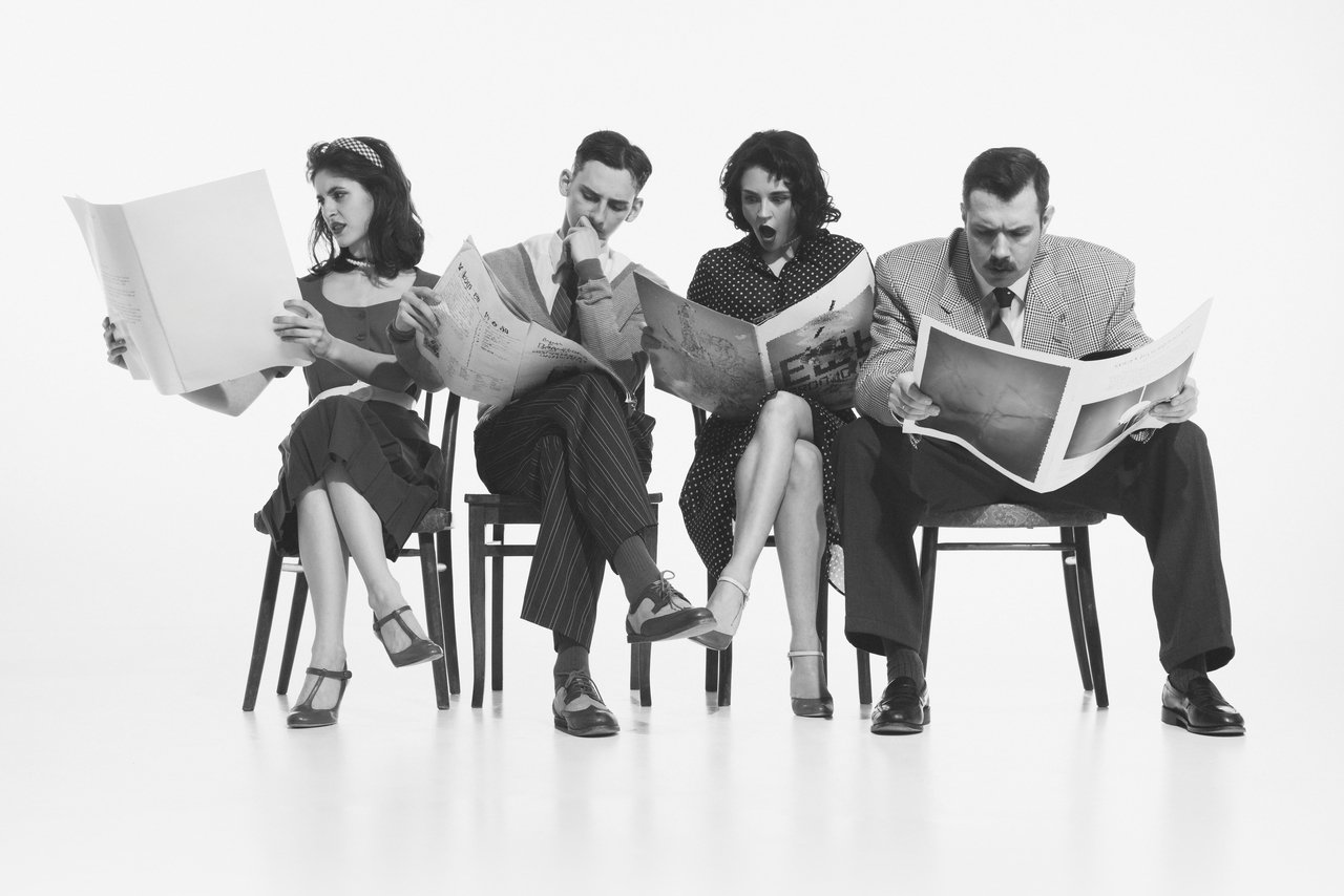 Four people sitting in chairs reading newspapers.